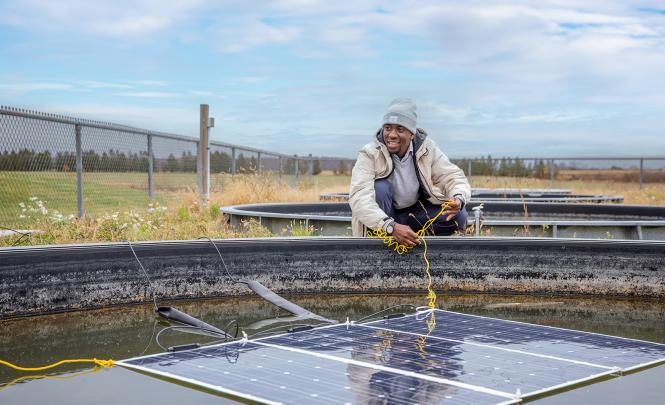 A researcher repositioning a solar panel floating in a water basin.