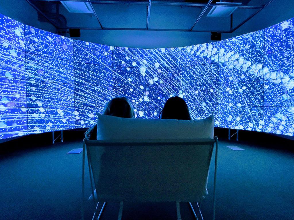 Two people sit in front of a curved video wall displaying illuminated renderings of satellites orbiting earth.
