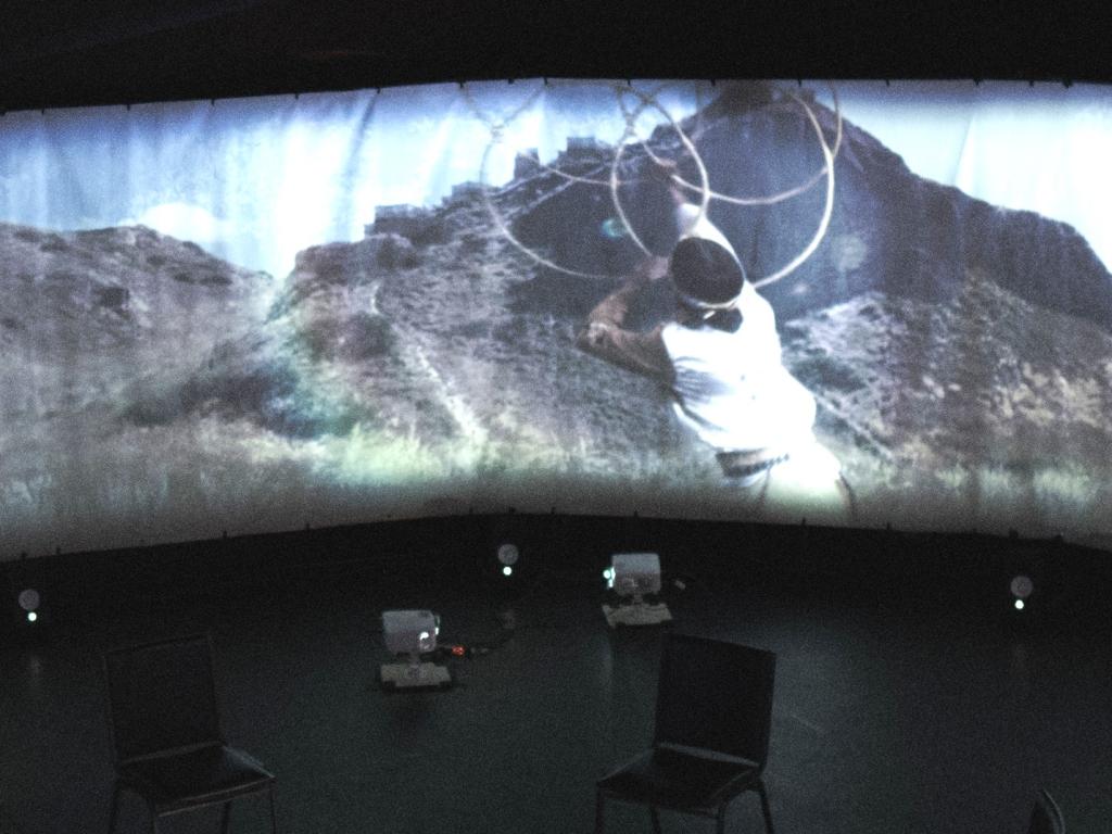 Sur un écran panoramique installé dans un grand espace circulaire, une personne danse avec des cerceaux.