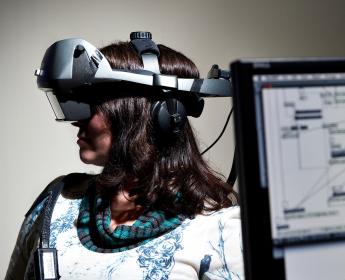 A person wears a headset covering their eyes with computer screen in foreground