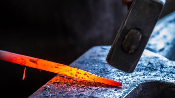 A stock photo of an iron rod being forged and hit with a big hammer.