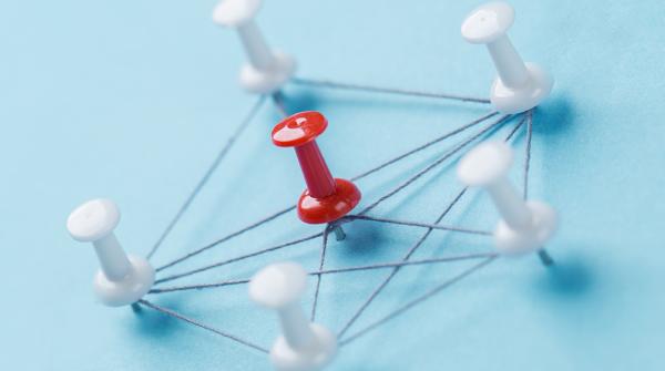 A stock image of a red pin on a pale blue background surrounded by a pentagon of five white pins, all connected with strings to form a geometric pentagon pattern.