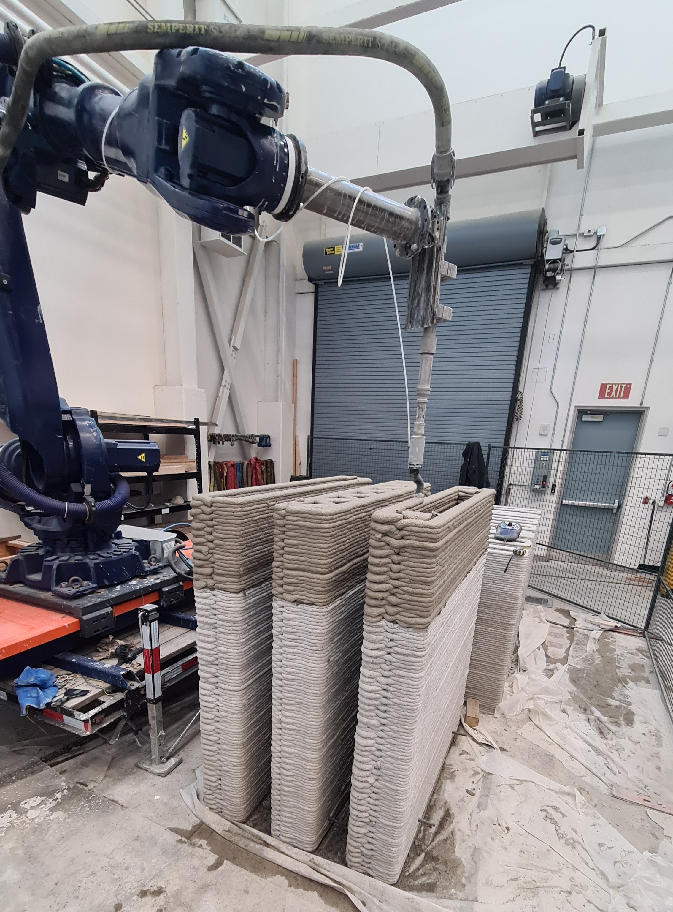 A robot arm suspended over three short cement walls.