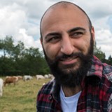 A man standing in a field with white and brown cows.