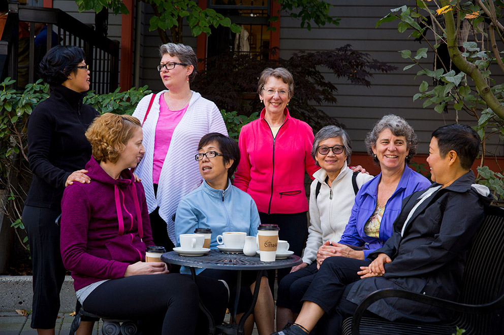 A crowd of people gathered around a table discussing and drinking coffee.