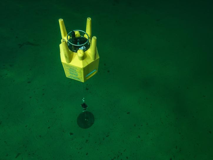 A floating bright yellow piece of equipment anchored to the ocean floor.