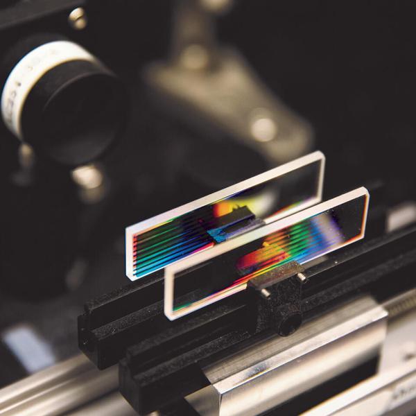 An apparatus holds two small rectangular glass slides with coloured lines.