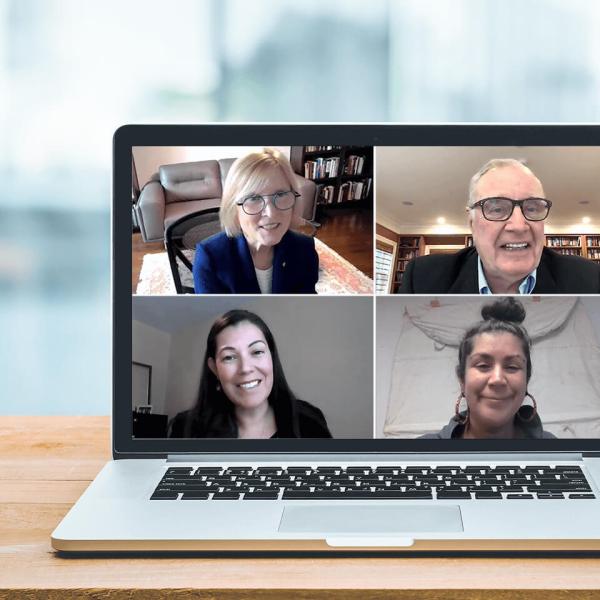 A laptop sitting on a desk shows four people in a virtual meeting.