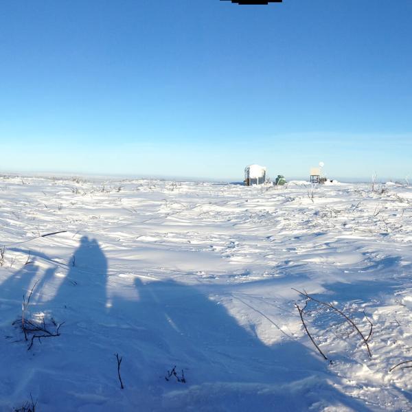 A panorama of a snowy, treeless landscape taken from on top of a snow machine with a meteorological tower and its guy-wires visible.