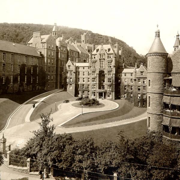 A grey and white photo of a multi-storeyed building with turrets at each corner and a large circular driveway in front.