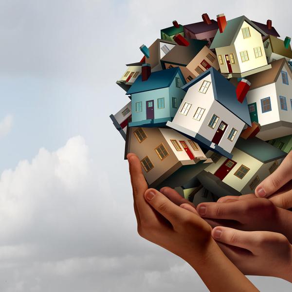 Several hands hold up an illustrated ball of houses against a cloudy sky.