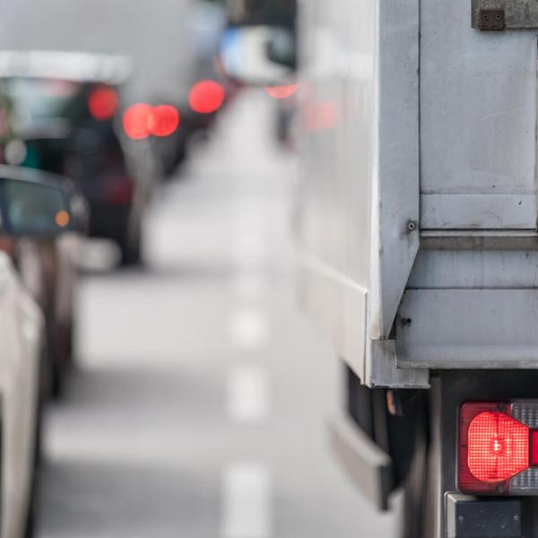 A close-up photo of taillights of a car and a transport truck at the back of a long line of traffic.