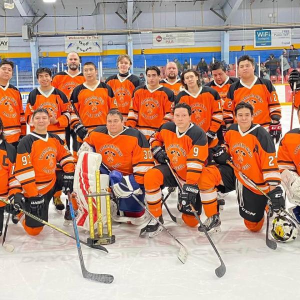 A hockey team in orange jerseys poses on the arena ice.