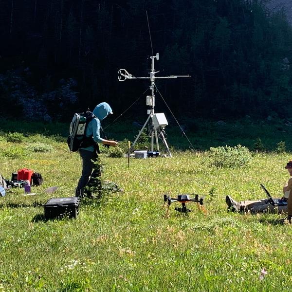 Trois personnes, l’une debout, l’autre accroupie et la troisième allongée dans une zone herbeuse, regardent leurs équipements de recherche : drones, antennes et ordinateurs en tout genre.