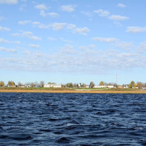 Low buildings and homes along a flat shoreline with water in the foreground. 