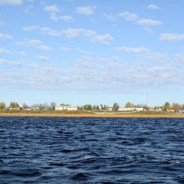 Ensemble de bâtiments bas et de maisons, le long d'un rivage plat. Au premier  plan se trouve de l'eau.