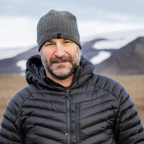 A person wearing a coat in an empty field, posing for a photo.