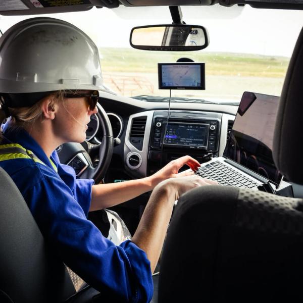 Assise derrière le volant d’un véhicule, une jeune chercheuse coiffée d’un casque de protection tape sur un ordinateur portable.