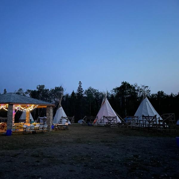 À l’extérieur, au crépuscule, un pavillon en pierre et plusieurs tipis sont disposés en cercle autour de gradins.