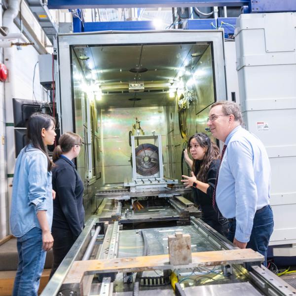 A group of people stand on either side of a long metal machine.
