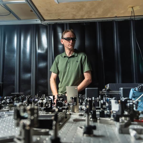 David Jones wears protective laser glasses as he stands behind a prototype on his lab bench.