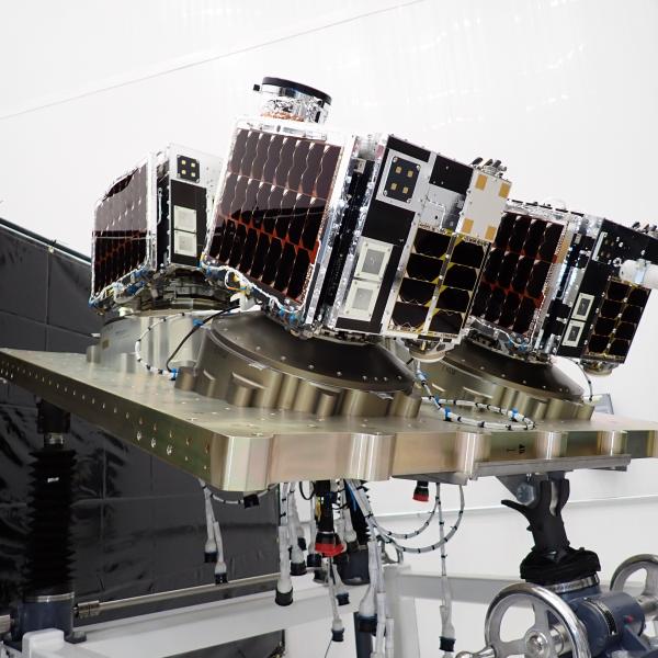 Three box-shaped satellites mounted on a metallic platform in a lab.
