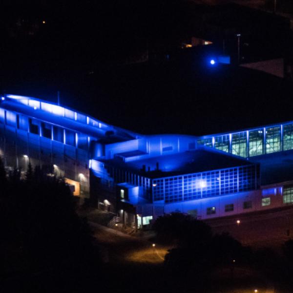 Vue nocturne, en plongée, d’un grand bâtiment dont les murs sont éclairés d’une vive lumière bleue.