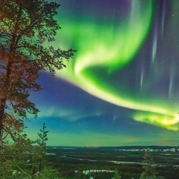 Un tourbillon de lumière verte dans le ciel au-dessus d’un paysage peu boisé.