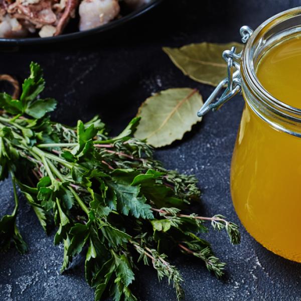 Un bocal de liquide jaune avec à côté, des herbes fraîches et un bol de grains de poivre