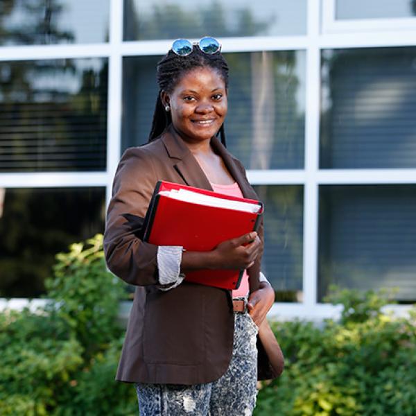 Jacqueline Mboko, an interpreter for London's Cross Cultural Learner Centre, holding a red binder posing for a photo outside.