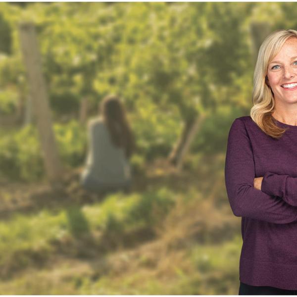 Heidi Fielding poses in front of a blurred image of a vineyard in the background