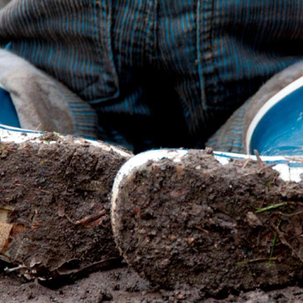 The soles of a child’s blue rubber boots, caked in mud