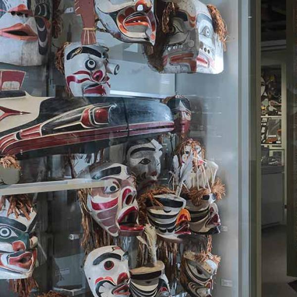 Une salle de musée peu éclairée compte de nombreux présentoirs affichant des masques autochtones peints de couleurs vives.