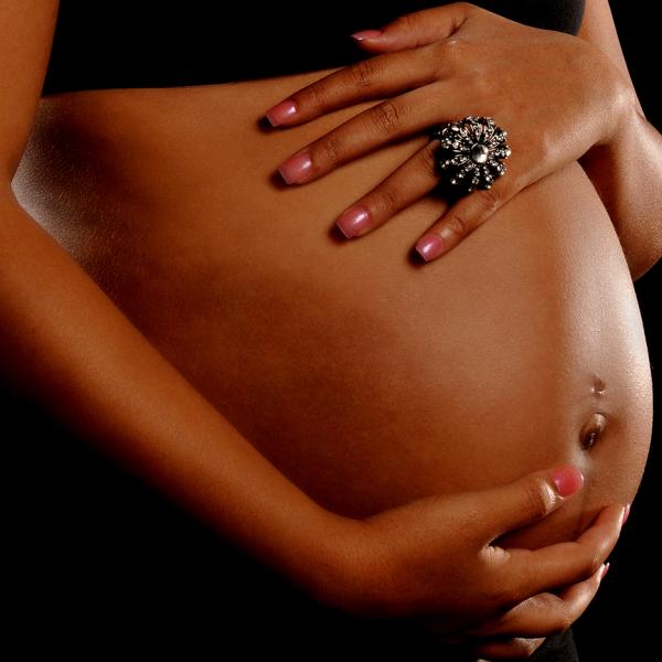 A close up shot of a woman’s hands on her pregnant stomach. 