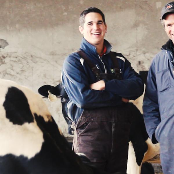 Albert and Logan Leyenhorst, father and son dairy farmers in Saskatchewan, posing with their herd in the barn.