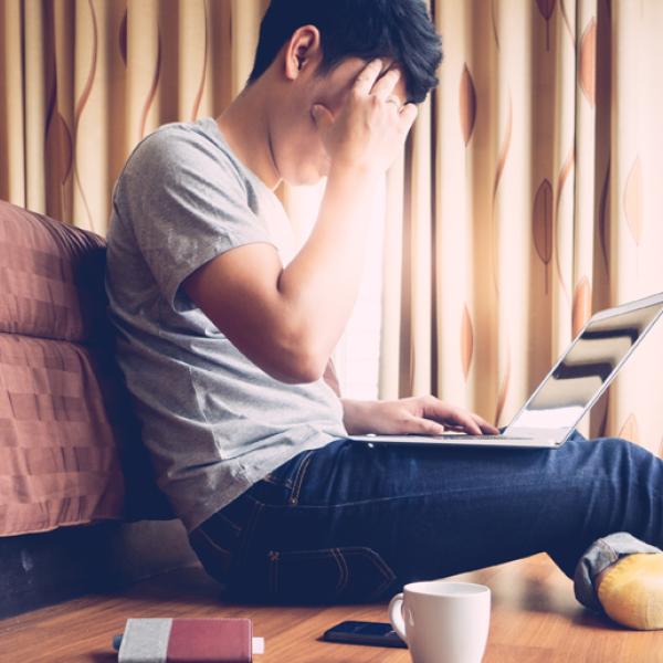 A person puts a hand to their forehead while sitting on the floor and looking at a laptop 