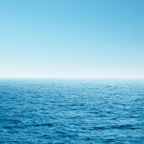 A thin white line on the horizon separates a wide expanse of blue ocean from a blue sky