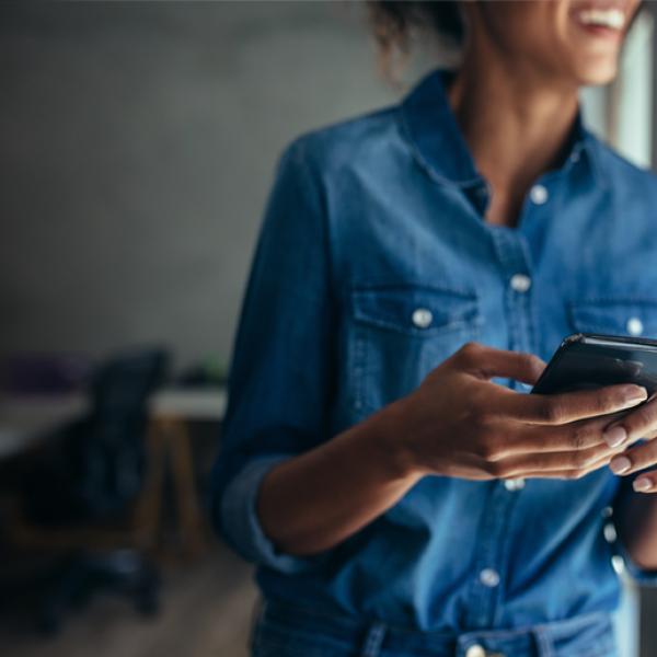 A woman, who is blurred out in the background, holds a mobile phone in the foreground