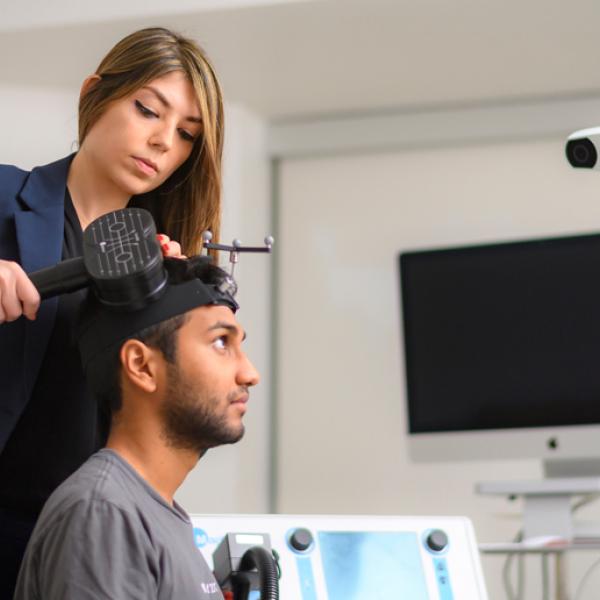 Faranak Farzan applies a device to the side of a seated man’s head