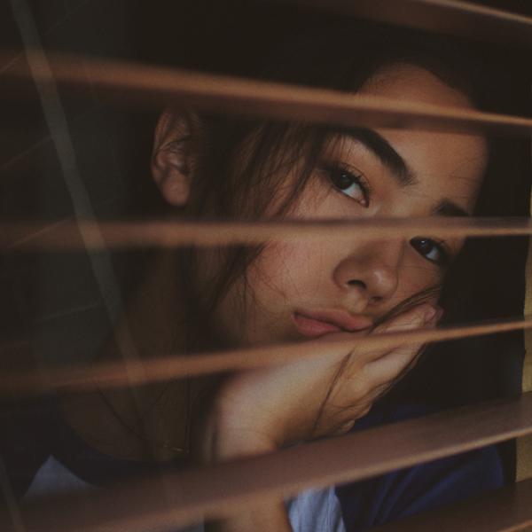 Young woman resting her face in her hand stares out a window through open shutters looking bored