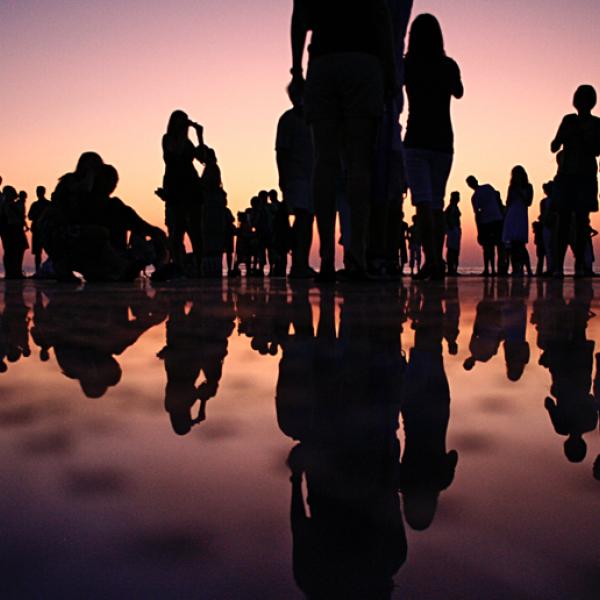 Silhouettes of many people interacting on a reflective surface that looks like water.