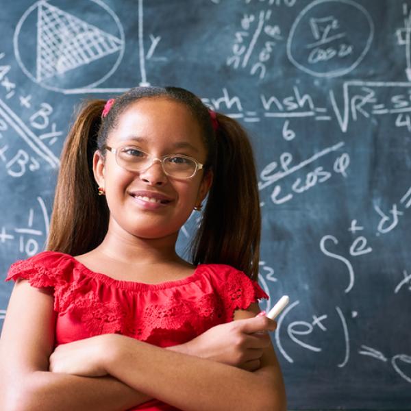 Pigtailed girl stands in front of chalkboard containing many mathematical