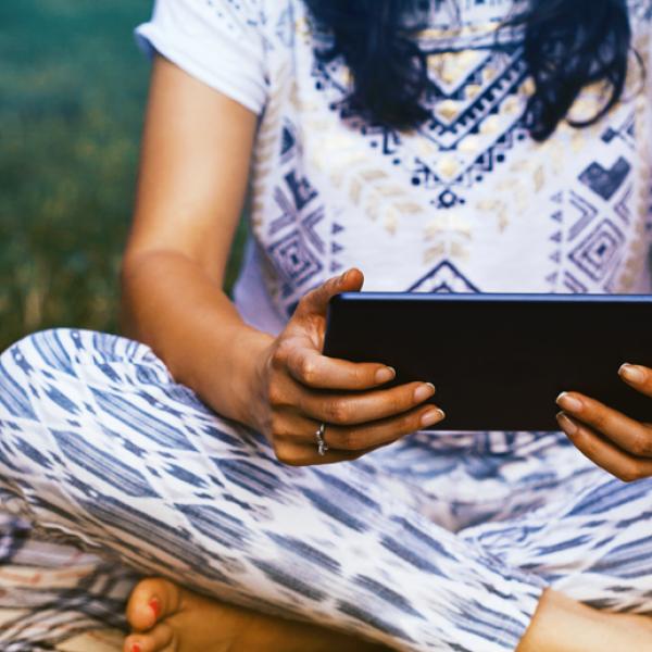 A woman sits cross-legged in the grass, holding an electronic tablet.
