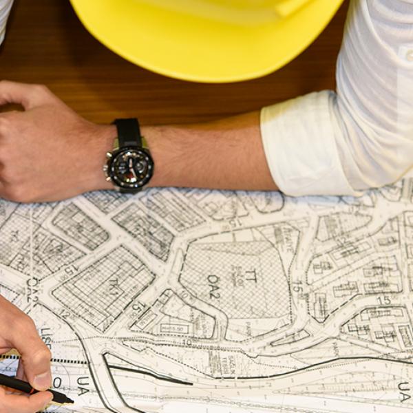 Vue du dessus d'une personne portant un chapeau de chantier jaune est penchée sur un plan de bâtiments posé sur une table en bois.