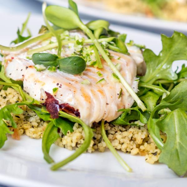 A plate of cooked sea bass fillet on a bed of arugula and couscous