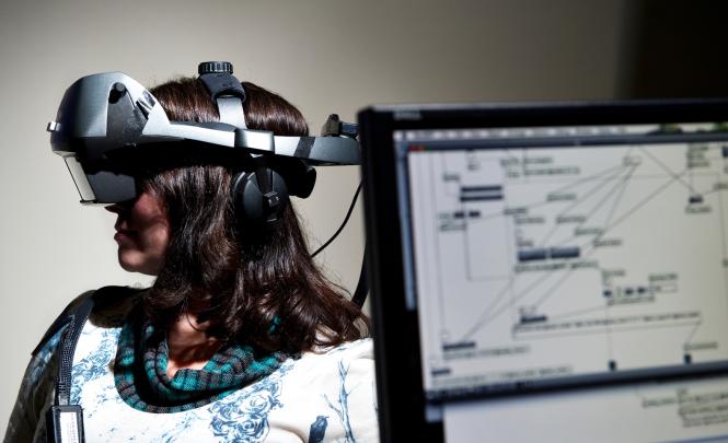 A person wears a headset covering their eyes with computer screen in foreground