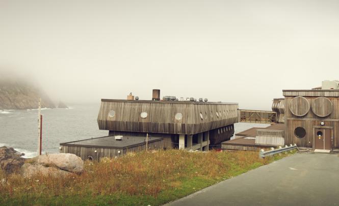 A wooden building with porthole windows on a rocky shoreline.