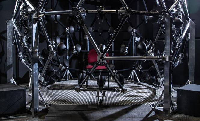Photo d'une chaise rouge positionnée au milieu d'une structure en acier en forme de dôme, munie de haut-parleurs, tous orientés vers le centre où se trouve la chaise.