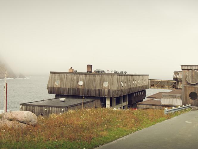 A wooden building with porthole windows on a rocky shoreline.
