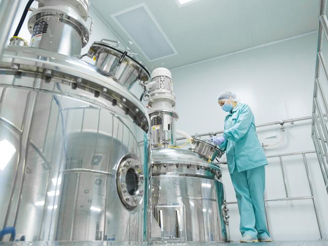 Une chercheuse portant des vêtements de protection manipule un appareil cylindrique en métal qui constitue une partie d'une plus vaste infrastructure de recherche